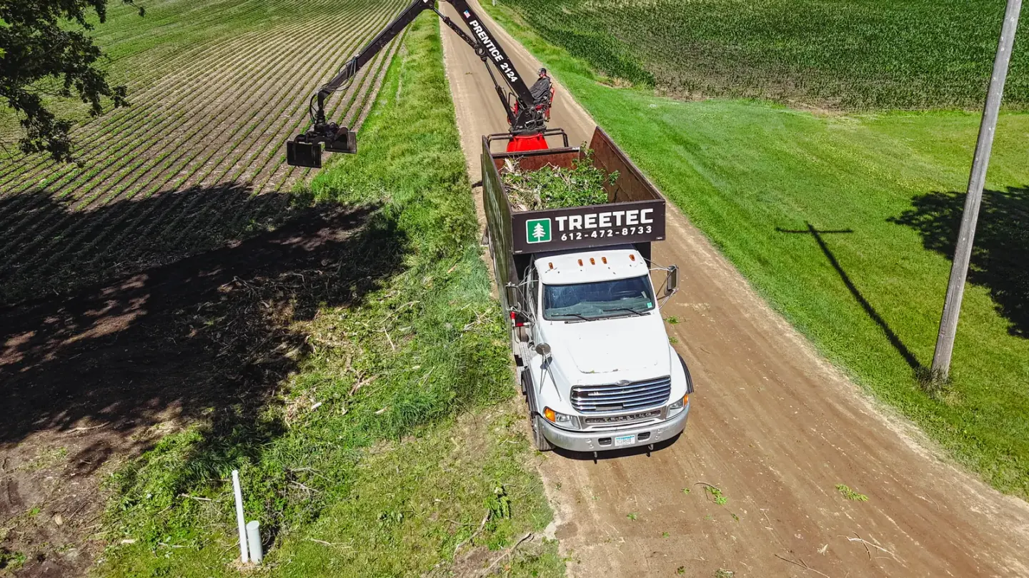Aerial view of a TreeTec grapple truck with the boom fully extended, loading brush on a field road in central Minnesota